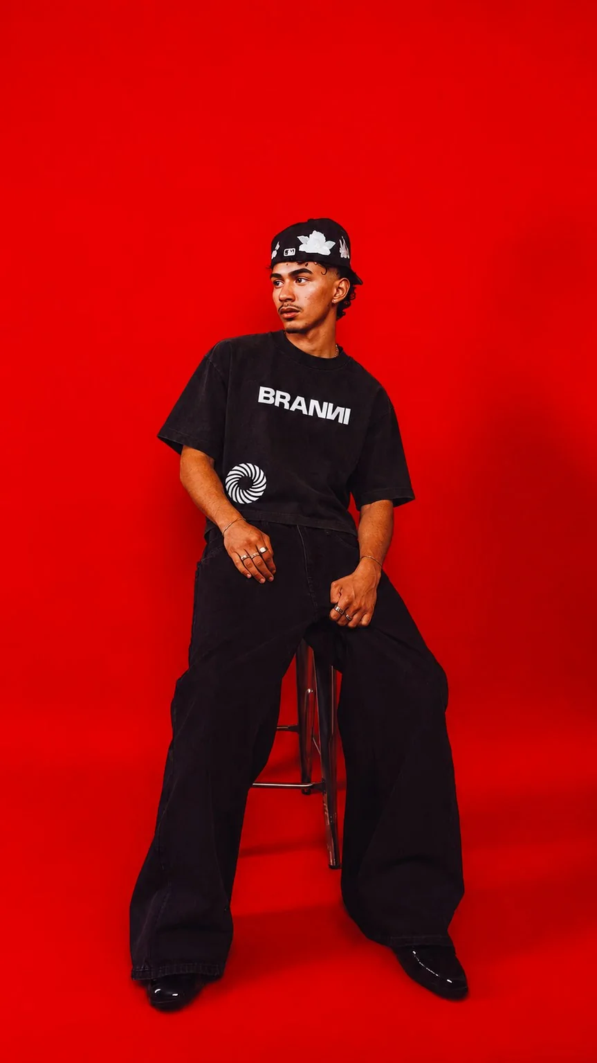 Model wearing a black BRANNI outfit against a red backdrop